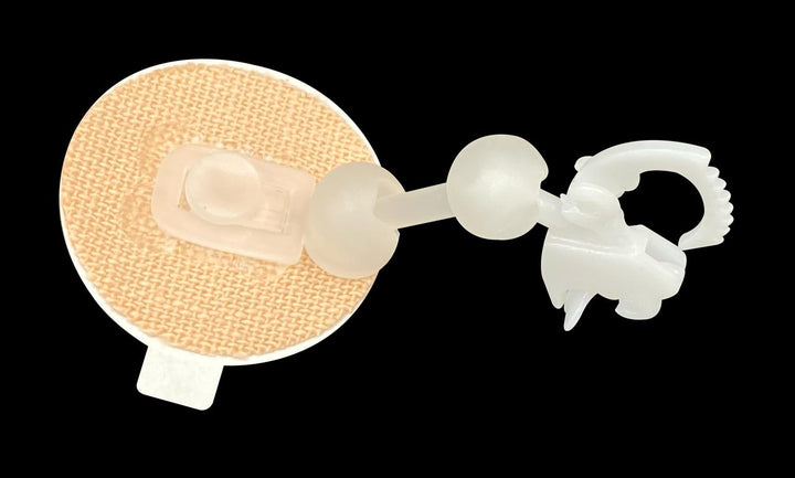 A beige, textured fabric patch features a white, clip-like Securement Device against a black background, highlighting the innovative design of beehive2u's Kosycare.