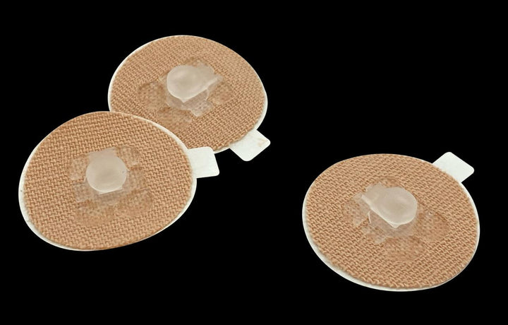 Three round adhesive patches, similar to the beehive2u Kosycare securement device, have raised gel centers on a black background.